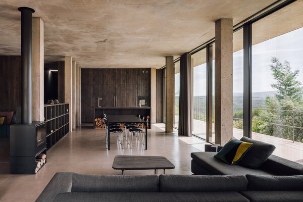 The open-space interior is divided by furniture and clusters of columns. Here, the kitchen flows into the dining and living room areas, heated by a wood-burning fireplace.